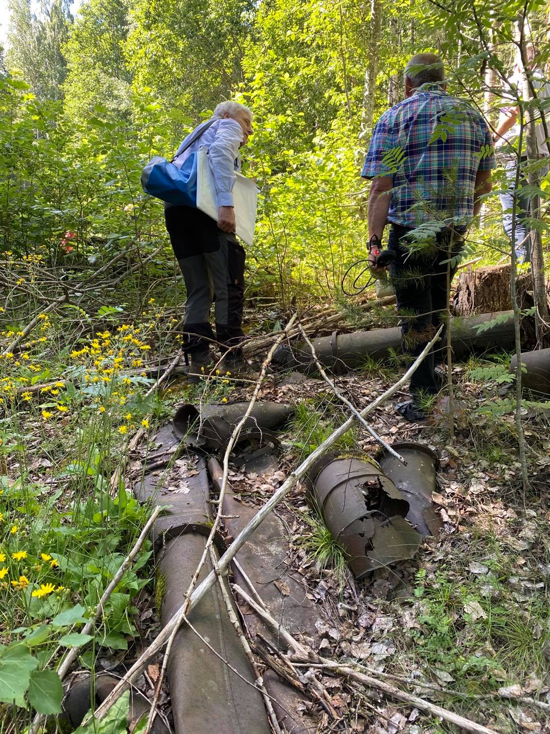 To personer står i skogen og ser på rester etter gamle rør fra Søve gruver.