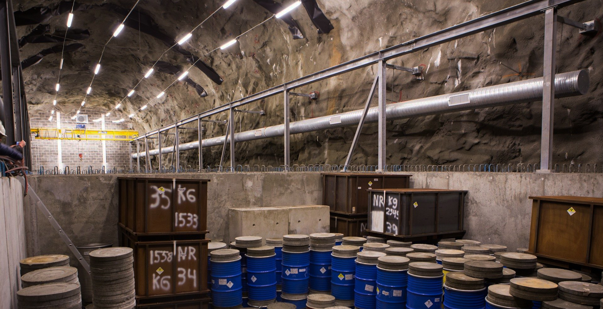 Bilde fra KLDRA, depot og lagringsplass for lav- og mellom-radioaktivt avfall. Grotte-rom med lysrør i taket og kasser/tønner langs gulvet.