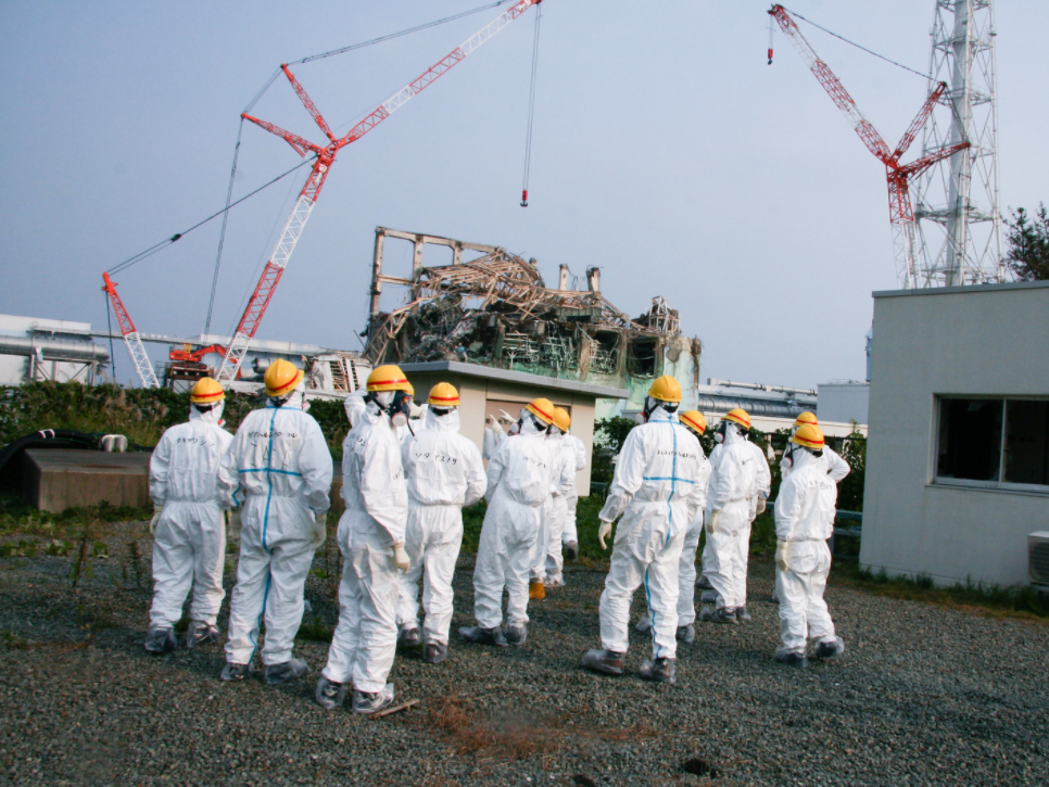 Bilde fra dekommisjonering av reaktor i Fukushima. Heisekraner som demonterer industribygg, mens 11 personer i verneutstyr ser på fra avstand. Giovanni Verlini / IAEA