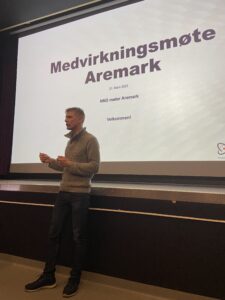 Mann står å presenterer foran en stor skjerm hvor det står "Medvirkningsmøte Aremark"