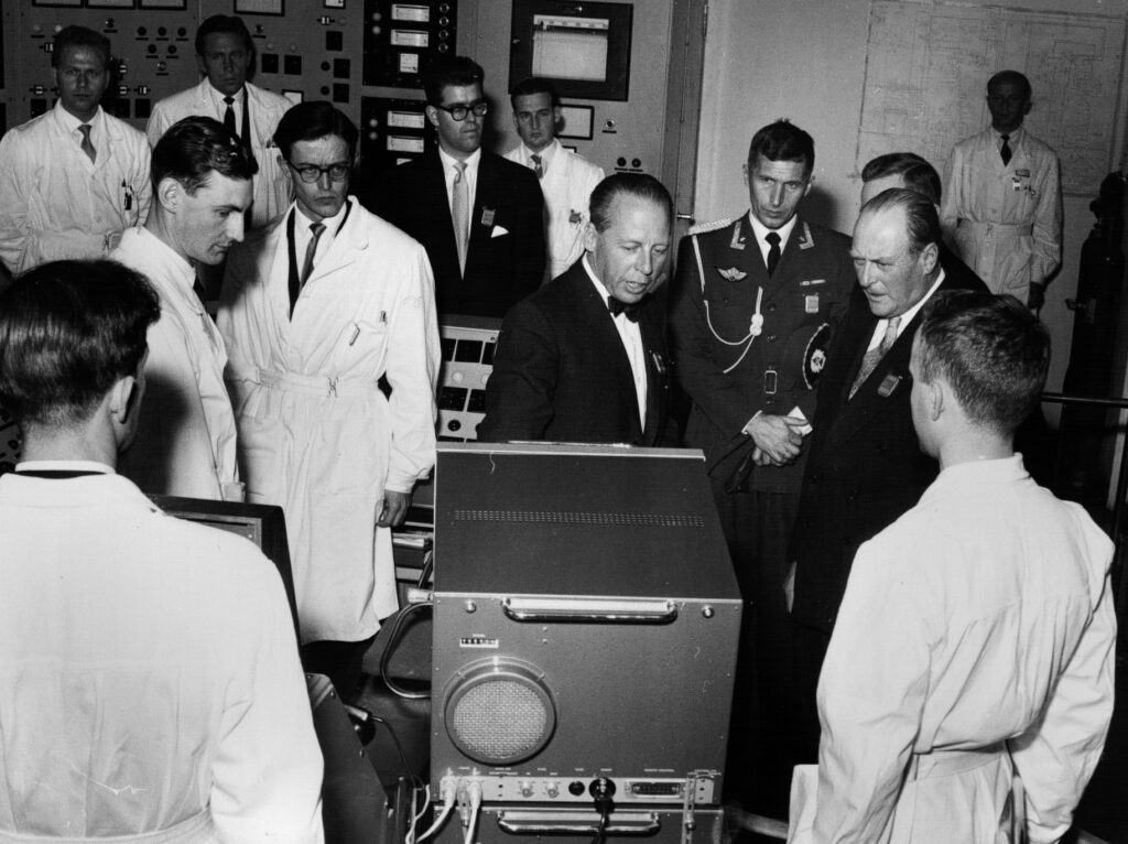 Kongen av Norge og menn samlet rundt teknisk utstyr inne i fjellet i Halden i forbindelse med åpningen av Haldenreaktoren i 1959.
