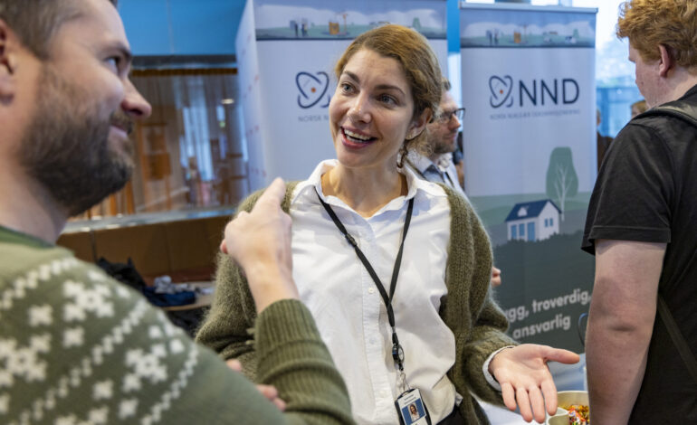 Kvinne som representerer Norsk Nukleær Dekommisjonering gestikulerer og snakker med student på stand under Karrieredagene på Høgskolen i Østfold.
