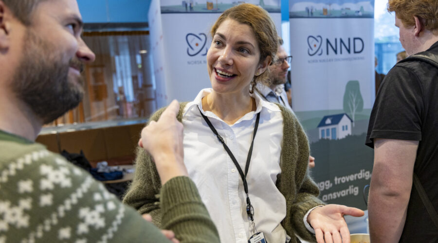 Kvinne som representerer Norsk Nukleær Dekommisjonering gestikulerer og snakker med student på stand under Karrieredagene på Høgskolen i Østfold.